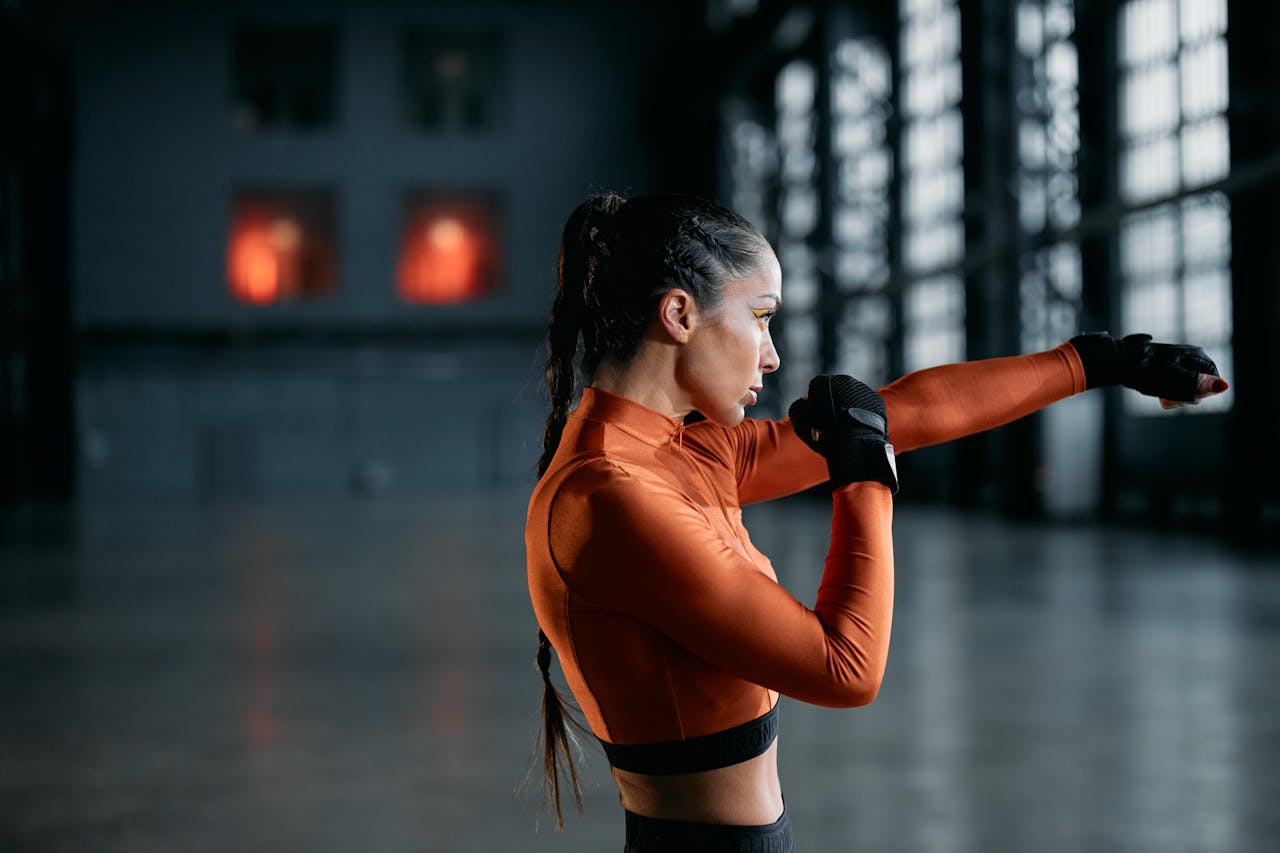 Side view of a woman in orange activewear practicing boxing indoors, exuding focus and determination.